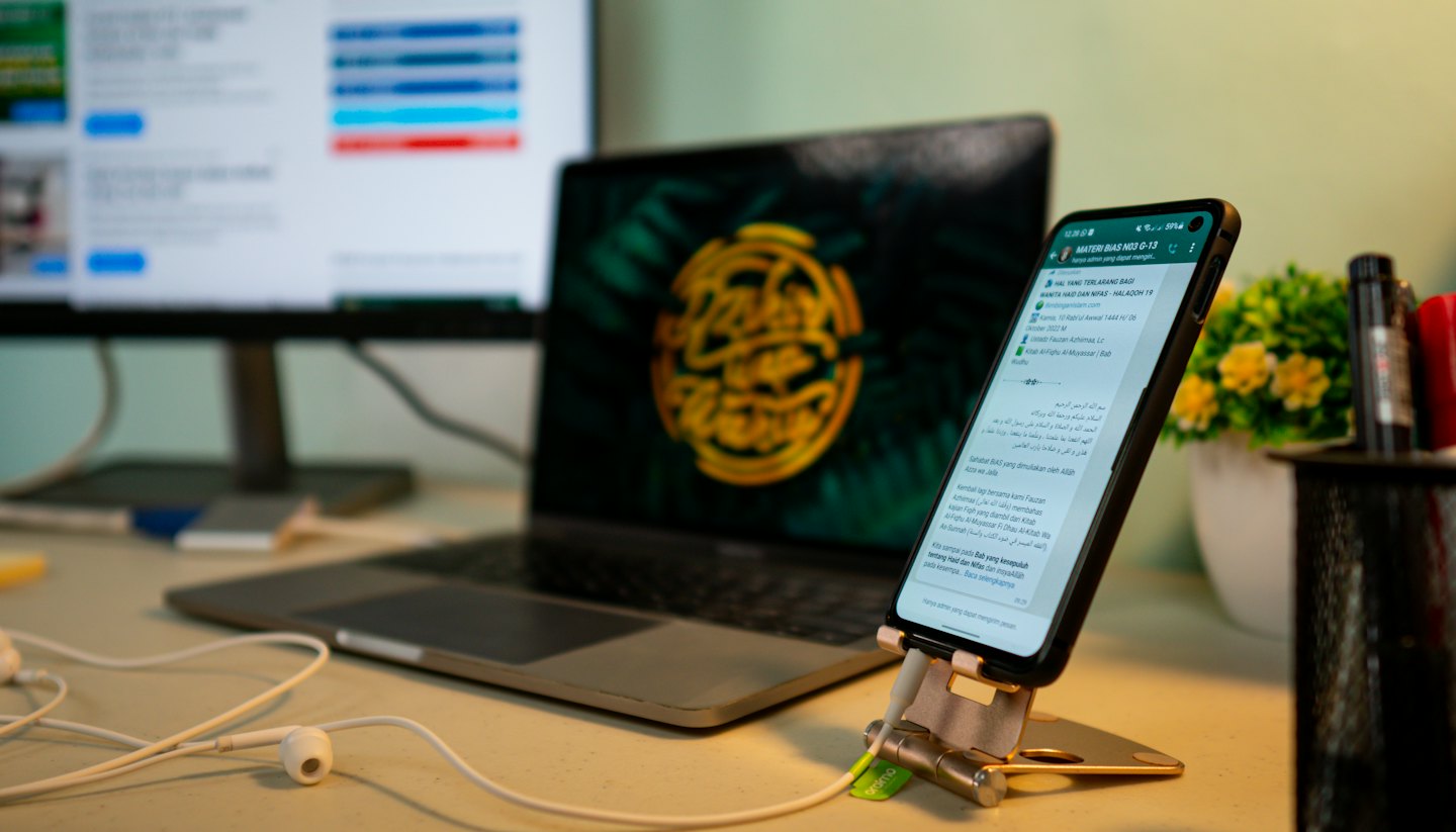 Un smartphone con texto en un idioma extranjero está sobre un soporte junto a un portátil.